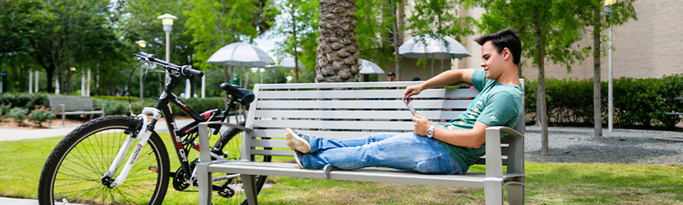 A USF student lying on a bench while using his tablet. 